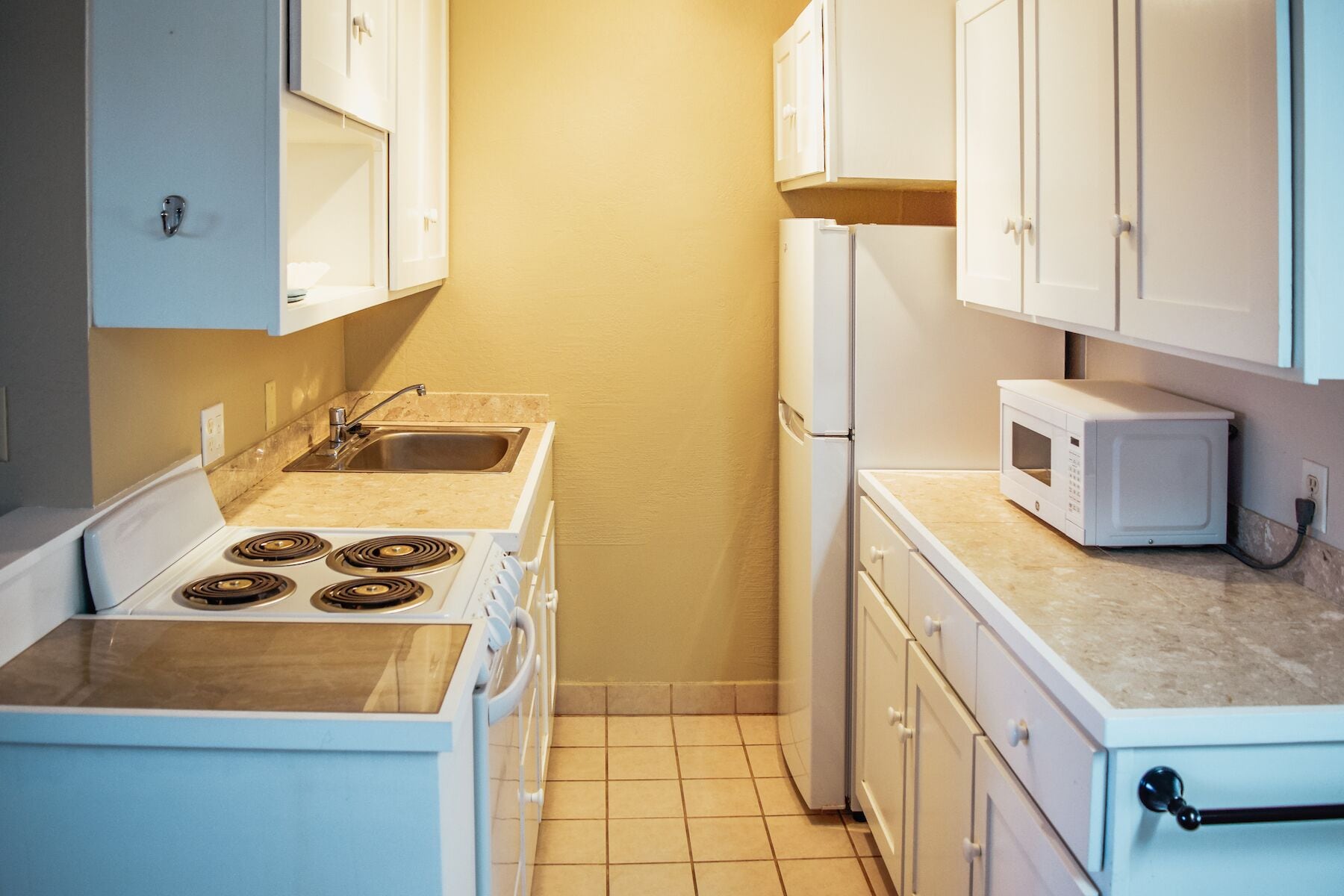 A compact kitchen with white cabinets, a stove, a sink, and a microwave.