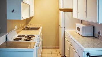 A compact kitchen with white cabinets, a stove, a sink, and a microwave.