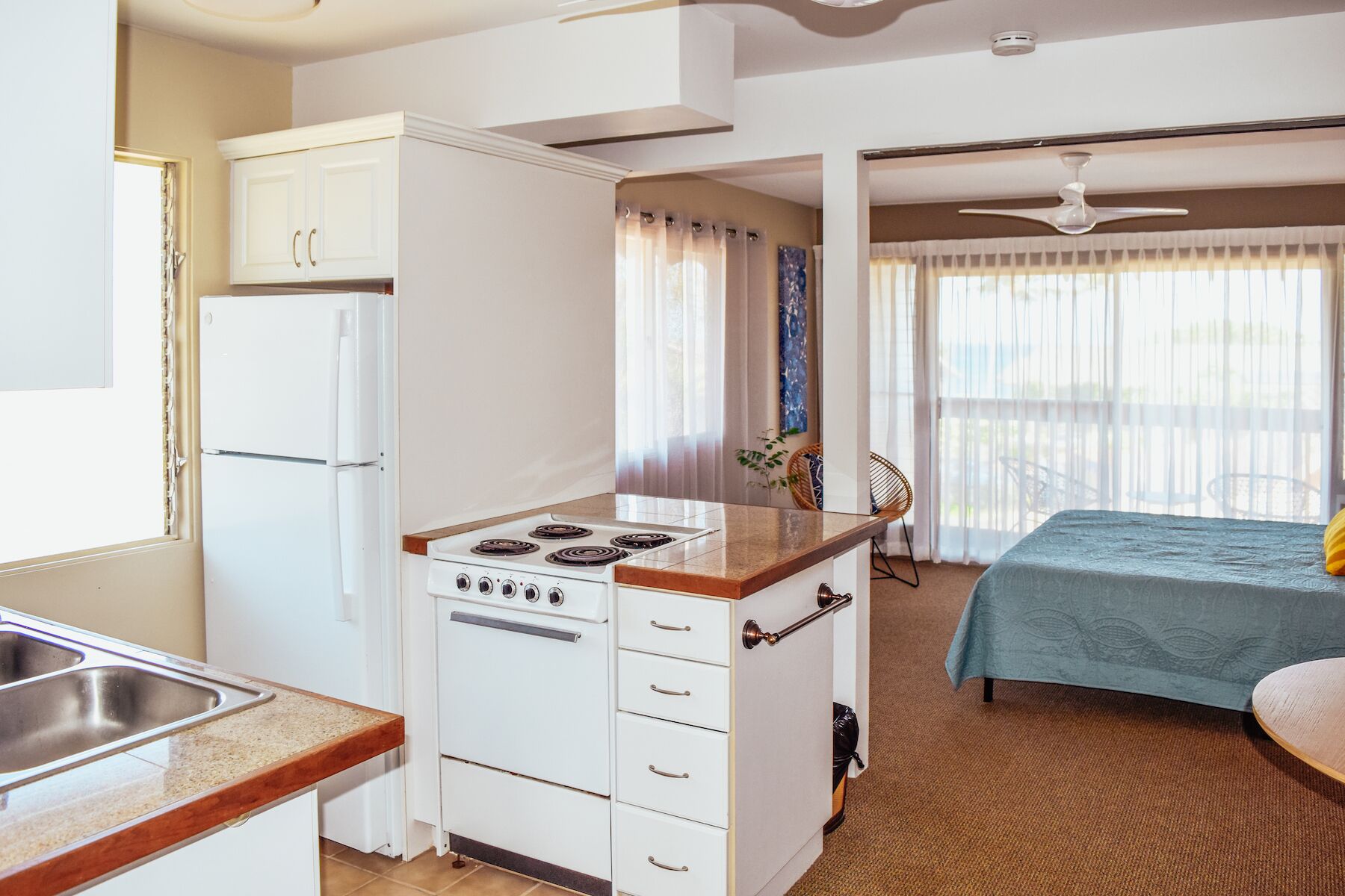 Une chambre d’hôtel compacte comprenant un coin cuisine, un lit et un balcon doté d’un ventilateur de plafond.