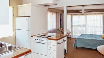 Ein kompaktes Hotelzimmer mit Küchenzeile, einem Bett und einem Balkon mit Deckenventilator.