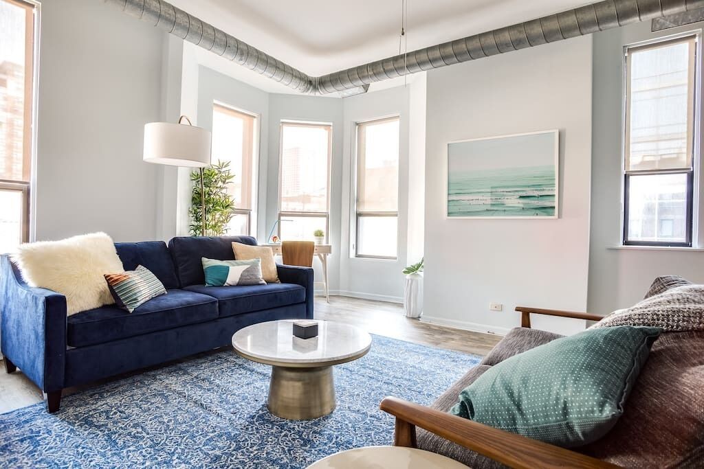 A living room with a blue sofa, a round coffee table, and a view of the city through large windows.