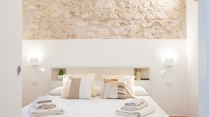 Ein Schlafzimmer mit einem großen Bett, weißer Bettwäsche und einer Wand aus strukturiertem Stein.