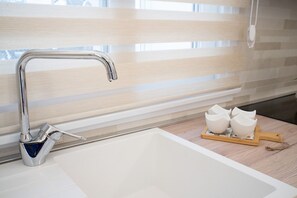 Een moderne keuken met een roestvrijstalen kraan, een witte wasbak en een houten snijplank met drie witte kommen.