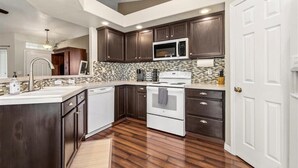 Une cuisine moderne avec des meubles de couleur bois foncé, une cuisinière blanche et un dosseret carrelé.