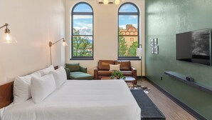 A modern hotel room with a large bed, a seating area with a sofa and armchair, a small table, and a TV mounted on the wall. - The Rathbone Hotel (Montrose)