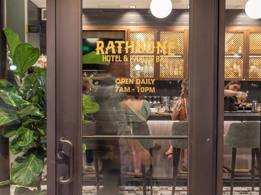 A hotel entrance with a sign reading "RATHBONE HOTEL & BAR" and "OPEN DAILY 7AM - 10PM".