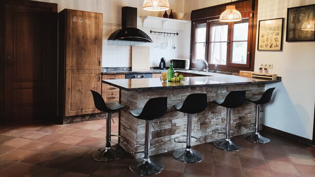 A kitchen with a central island, bar stools, a wooden cabinet, a microwave, and hanging utensils.