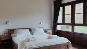 A wooden bed with white linens, a nightstand with a clock, and a window with curtains.