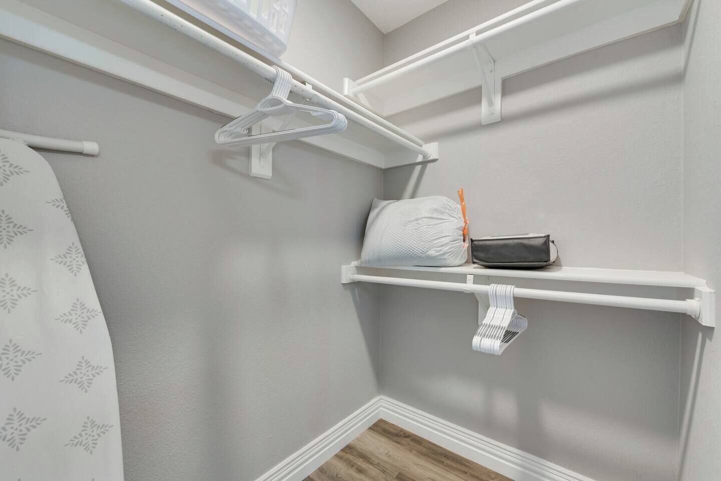 A closet with white shelves, a hanging rack, and a wooden floor.