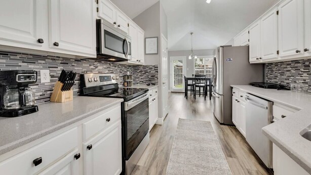A modern kitchen with white cabinets, a black stove, a microwave, and a coffee maker.