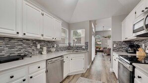 A modern kitchen with white cabinetry, a tiled backsplash, and a central island. - Updated, Comfortable, and Quiet Space close to DFW International Airport! (Coppell)