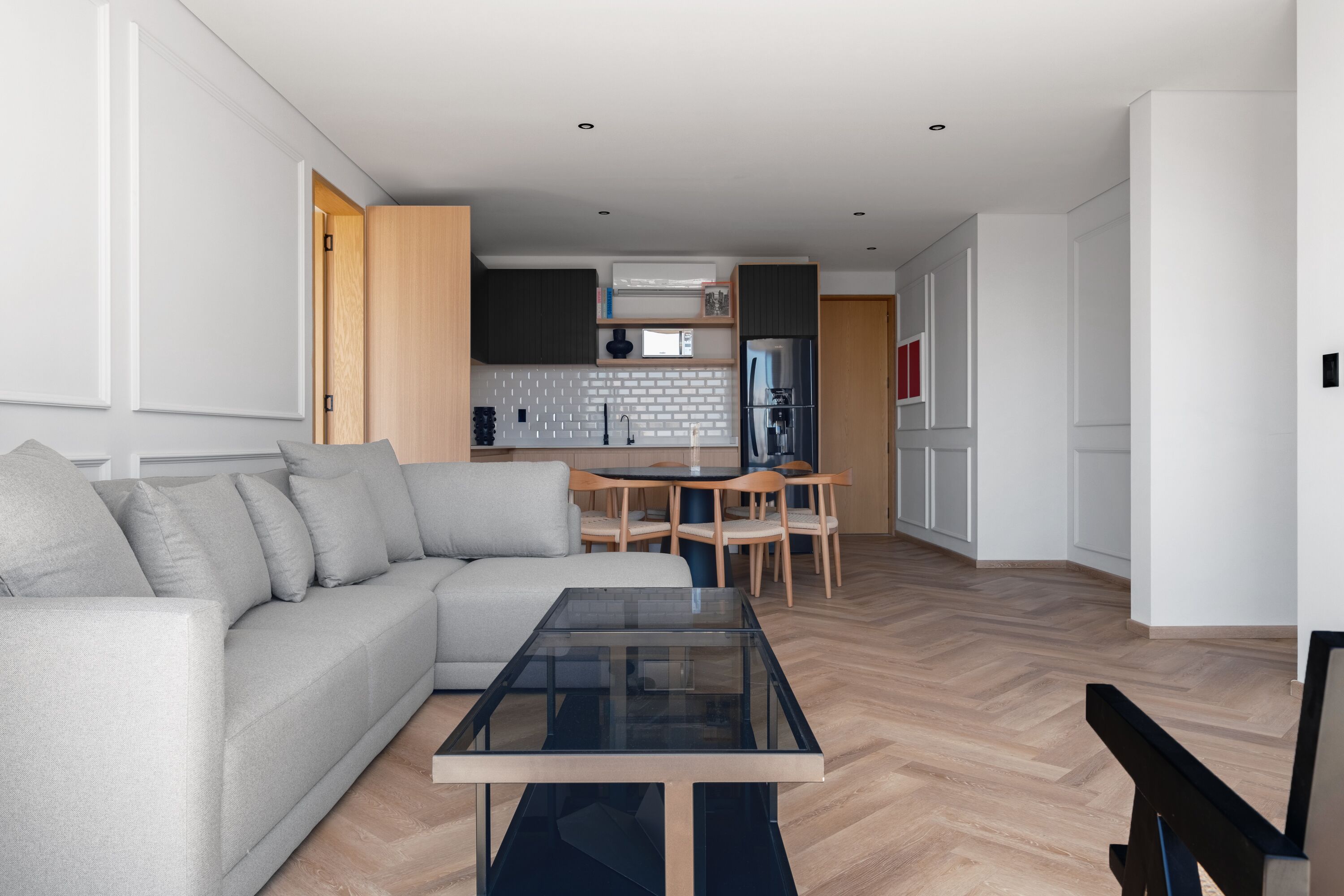Uma sala de estar moderna com um sofá, uma mesa de centro de vidro e uma área de jantar com mesa e cadeiras.