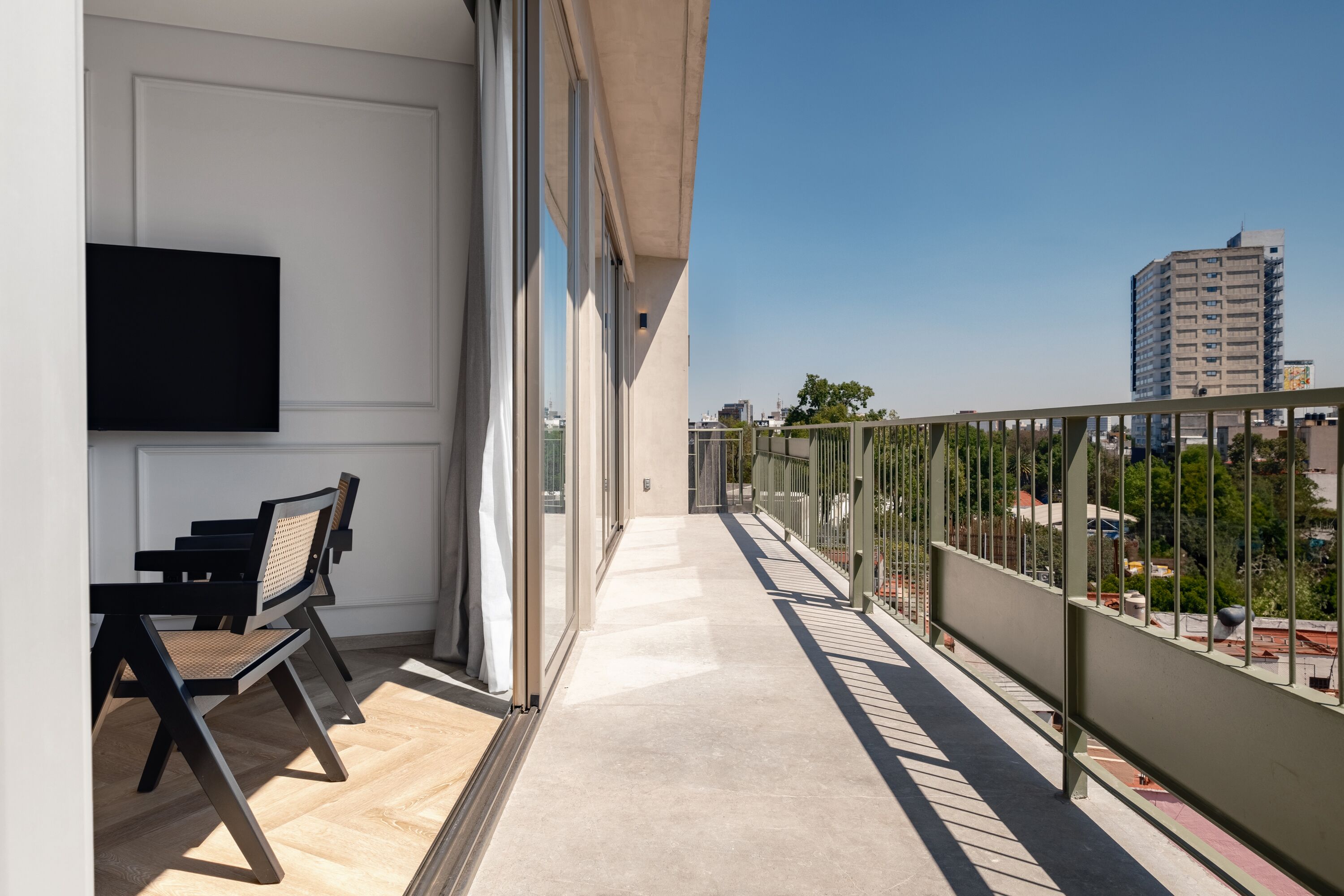 A balcony with a seating area, a TV mounted on the wall, and a view of the cityscape.