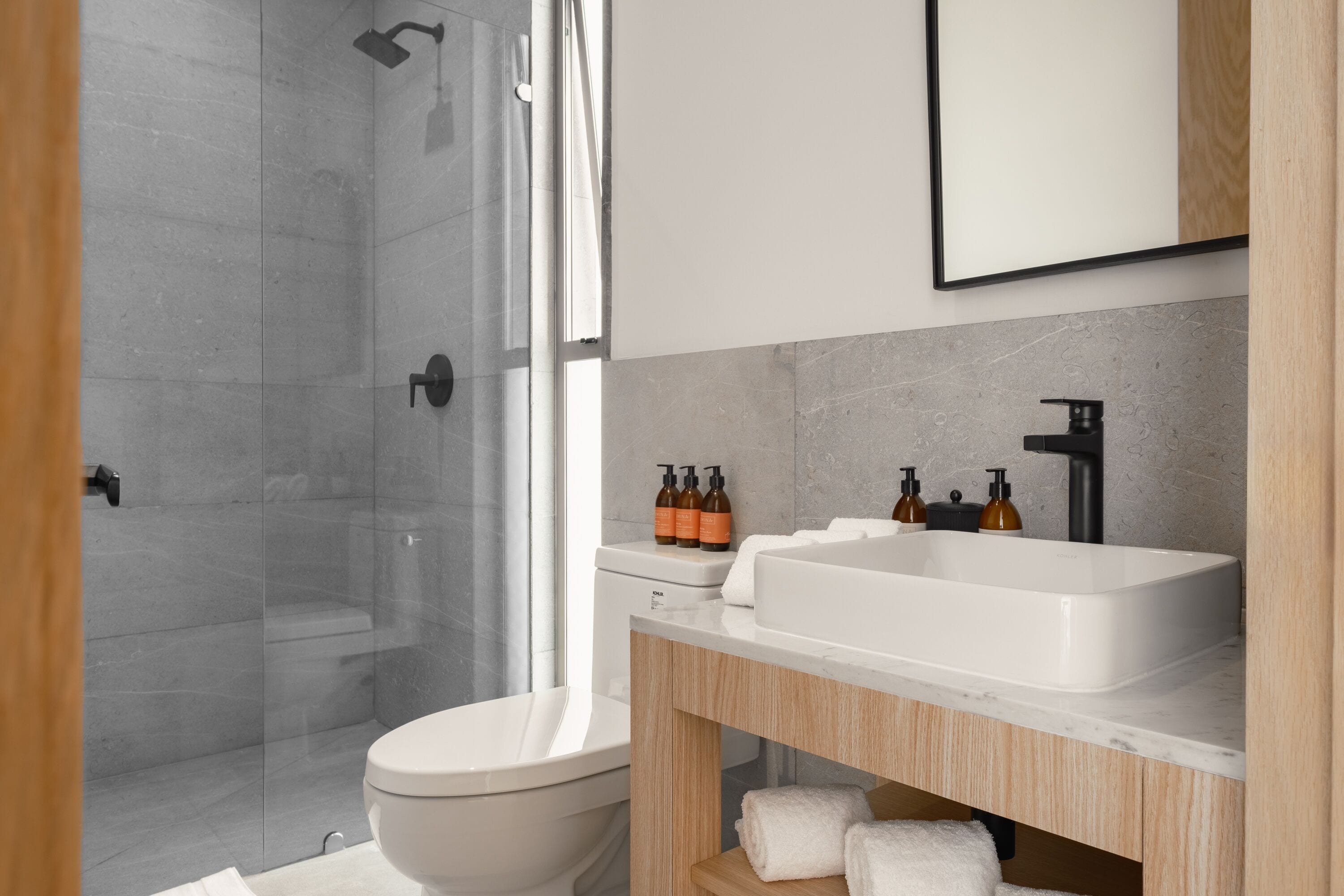 A modern bathroom with a glass shower enclosure, a white toilet, a sink with soap dispensers, and a mirror above the sink.