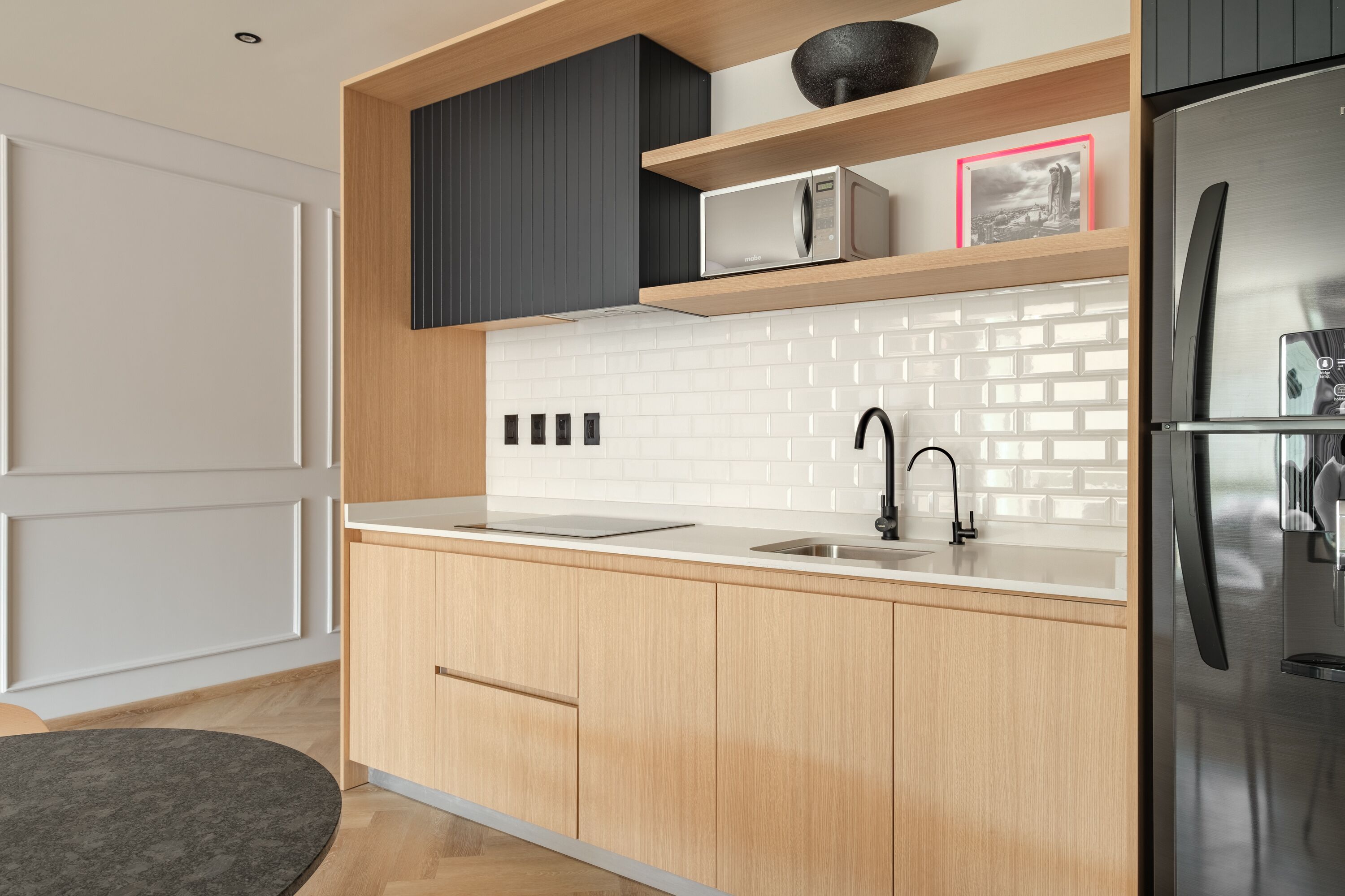 A modern kitchen with wooden cabinets, a white tiled backsplash, a stainless steel refrigerator, and a black faucet.