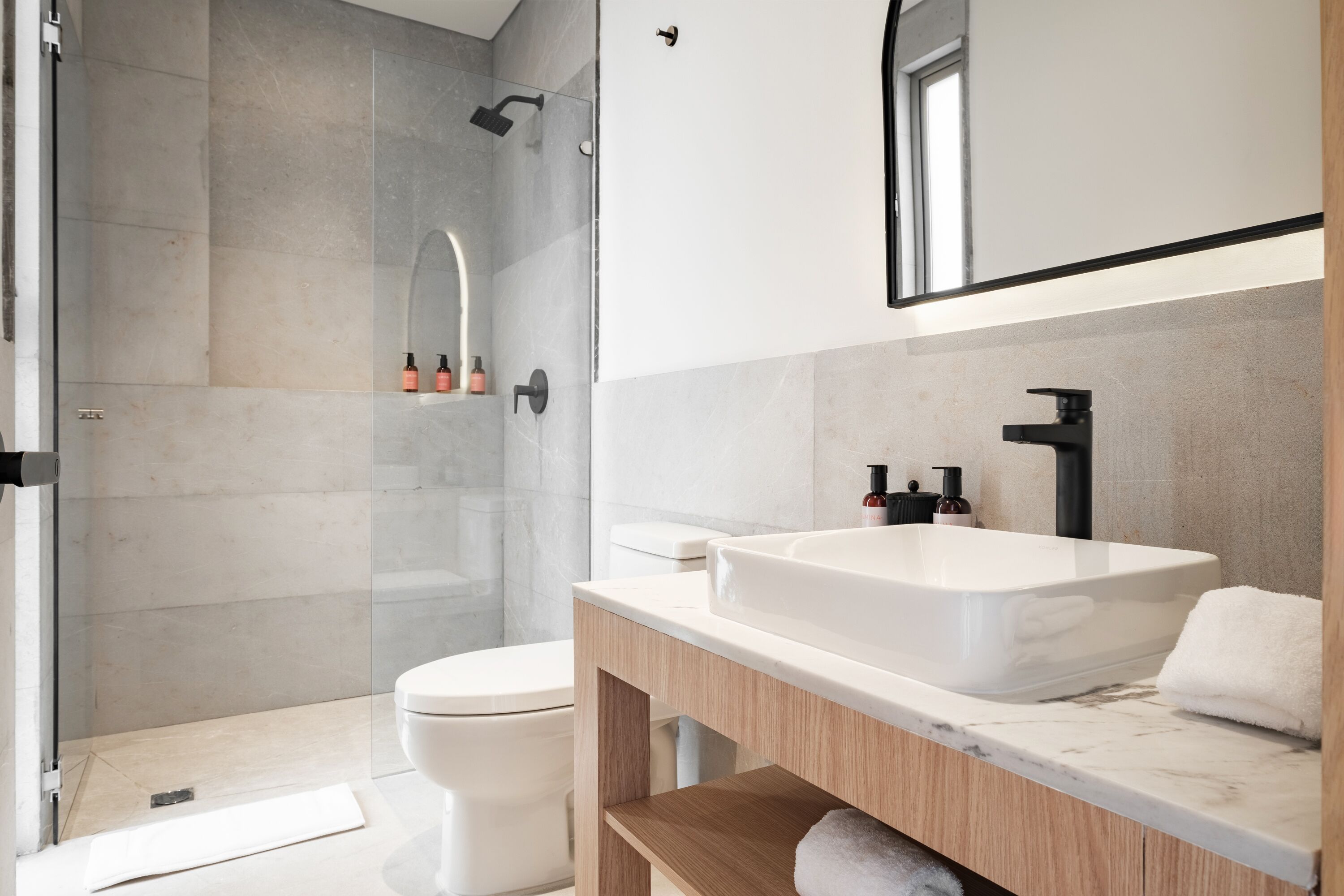 A modern bathroom with a glass shower enclosure, a white toilet, and a marble vanity with a large sink.
