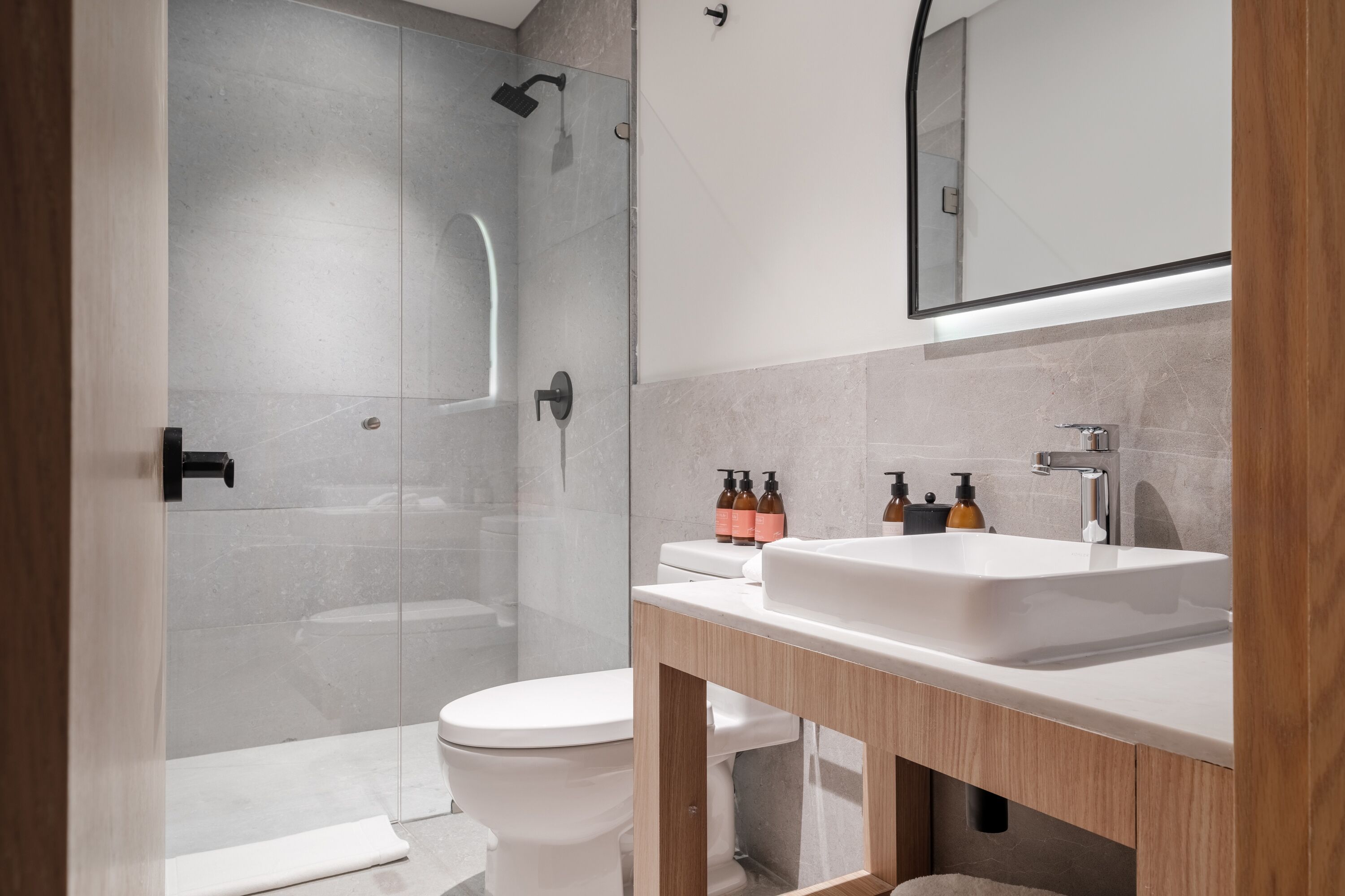 A modern bathroom with a glass-enclosed shower, a white toilet, and a wooden vanity with a sink.