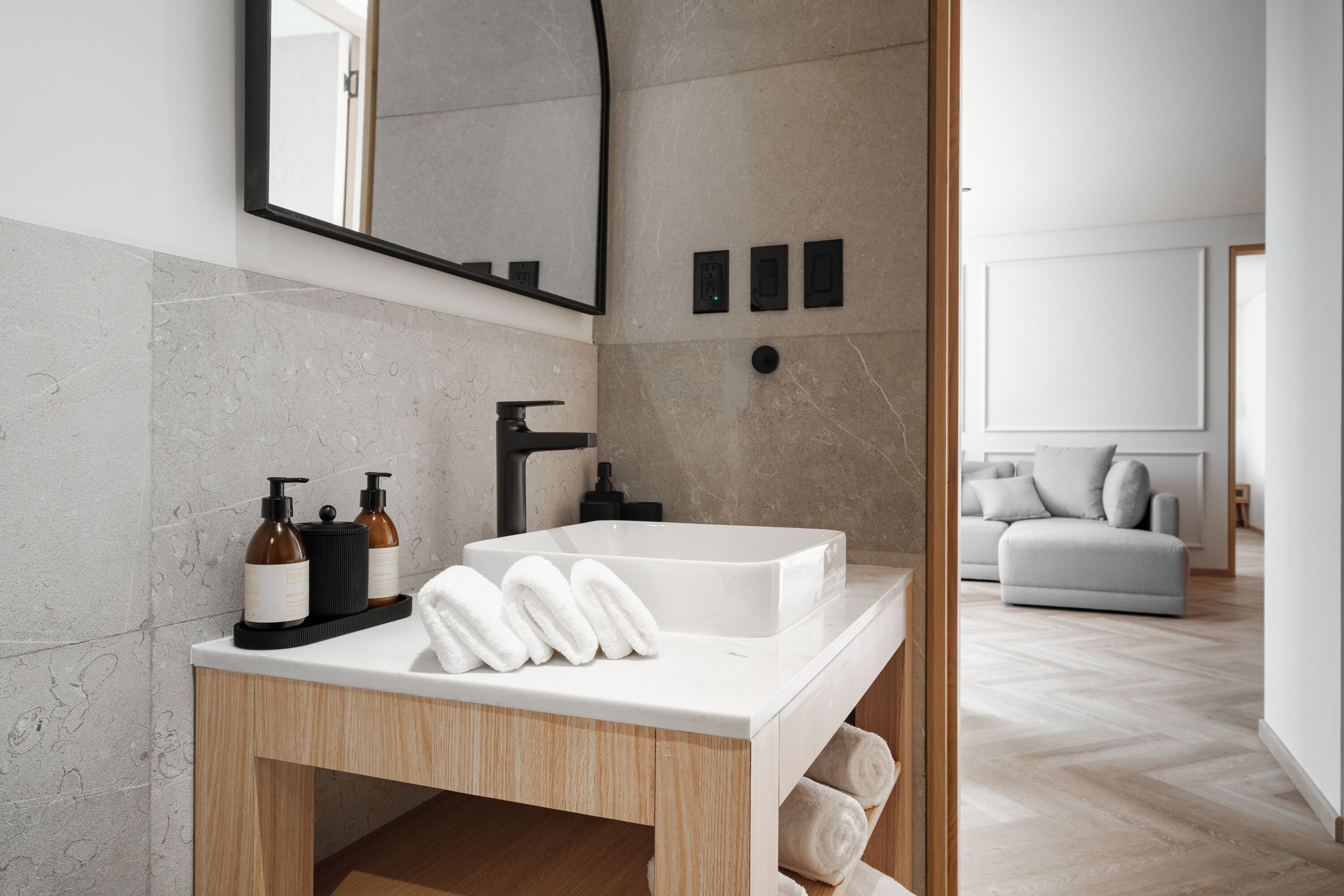 Une salle de bain moderne avec un grand lavabo blanc, un meuble-lavabo en bois et un miroir au-dessus. On y trouve des serviettes et des articles de toilette sur le meuble-lavabo.