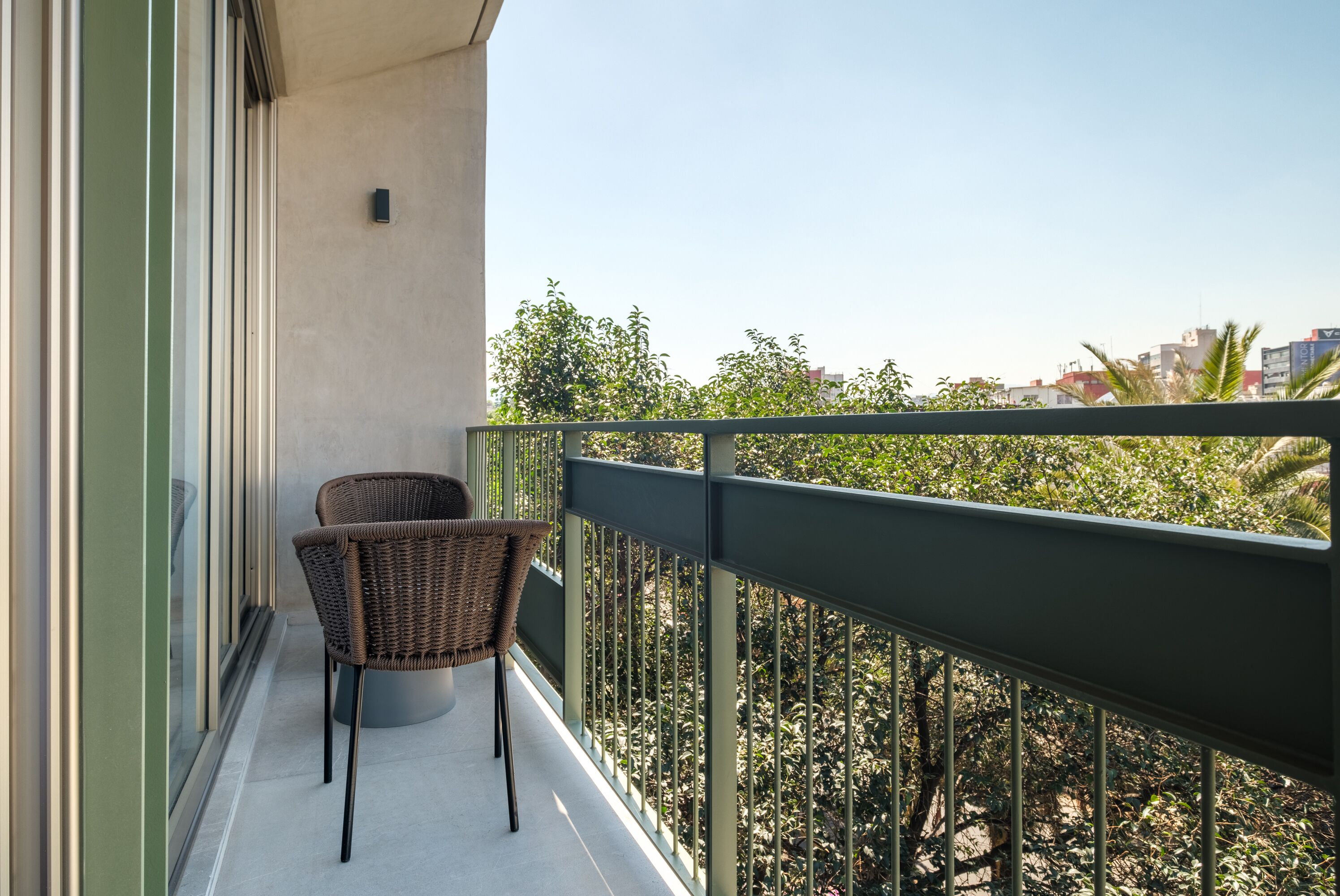Ein Balkon mit zwei Korbstühlen und Blick auf eine Stadtlandschaft mit Bäumen.
