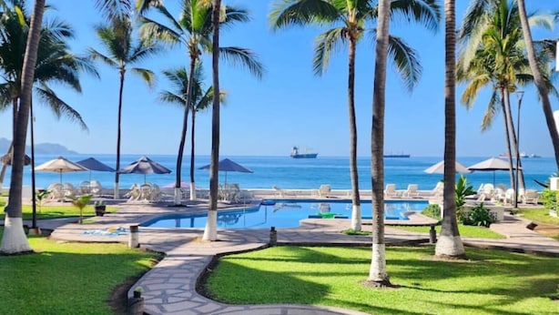 A resort pool area with palm trees, lounge chairs, and a view of the ocean. - Departamento Frente a la Playa, Salagua Manzanillo (Manzanillo)