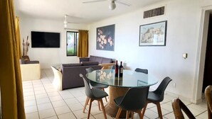 A modern living room with a glass dining table, grey sofas, and a flat-screen TV. - Departamento Frente a la Playa, Salagua Manzanillo (Manzanillo)