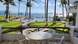 A balcony with a view of a pool area, palm trees, and a distant ship. - Departamento Frente a la Playa, Salagua Manzanillo (Manzanillo)