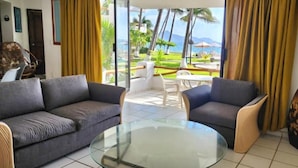 A living room with two sofas, a glass coffee table, and a view of a tropical outdoor area with palm trees and a pool. - Departamento Frente a la Playa, Salagua Manzanillo (Manzanillo)