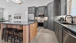 Una cocina moderna con armarios grises, una isla central con taburetes, electrodomésticos de acero inoxidable y una lámpara colgante.