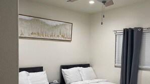 A hotel room with two beds, a ceiling fan, a painting on the wall, and a window with curtains.