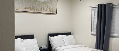 A hotel room with two beds, a ceiling fan, a painting on the wall, and a window with curtains.