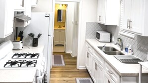 A narrow kitchen with white cabinets, a microwave, a sink, and a stove.
