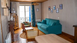 A cozy living room with a teal sofa, a wooden coffee table, a wicker chair, and a bookshelf.