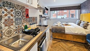 Een compacte keuken met een spoelbak en fornuis, een bed met uitzicht en een klein eethoekje.