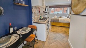 Een compact appartement met kitchenette, eethoek en een slaapkamer met bed en raam.