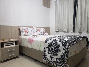 A neatly made bed with floral and patterned bedding, a bedside table with a wood box, and a window with curtains.
