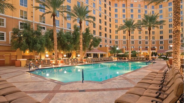 A hotel pool area with lounge chairs, palm trees, and a large building in the background. - 3Bed/2Bath Vegas Paradise at Grand Desert!! (Las Vegas)