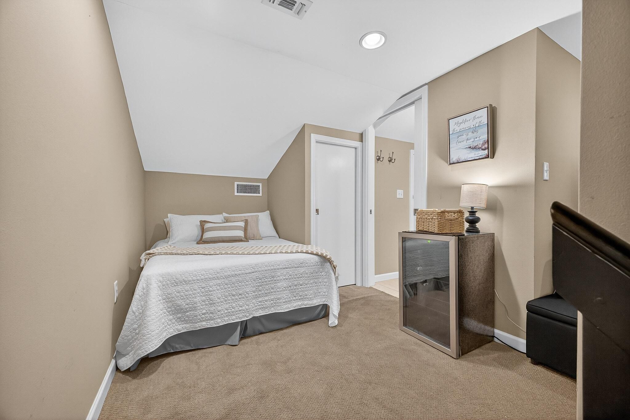 Une chambre à coucher avec un lit, une commode, une lampe et une citation encadrée accrochée au mur.