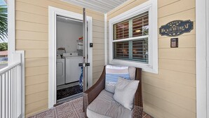 A covered porch with a wicker chair, a washing machine, and a sign reading "Sandy's Beach Retreat." - Sandy's Beach Retreat (Miramar Beach)