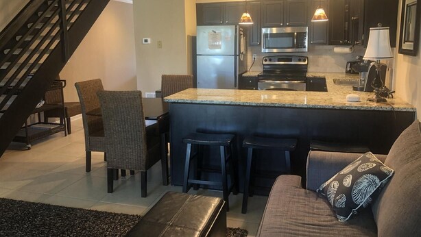 A modern kitchen with dark cabinets, stainless steel appliances, and a central island with bar stools. - Sandy's Beach Retreat (Miramar Beach)