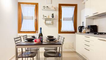 A dining area with a table set for two, a bottle of champagne, and a bag of snacks.