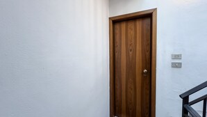 Een houten deur met een koperen handgreep, een witte muur en een zwarte balustrade.