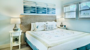 A bedroom with a bed, two bedside tables, a nightstand, a wall-mounted lamp, a potted plant, and a window with blinds. - 2C, Stay Salty (Miramar Beach)