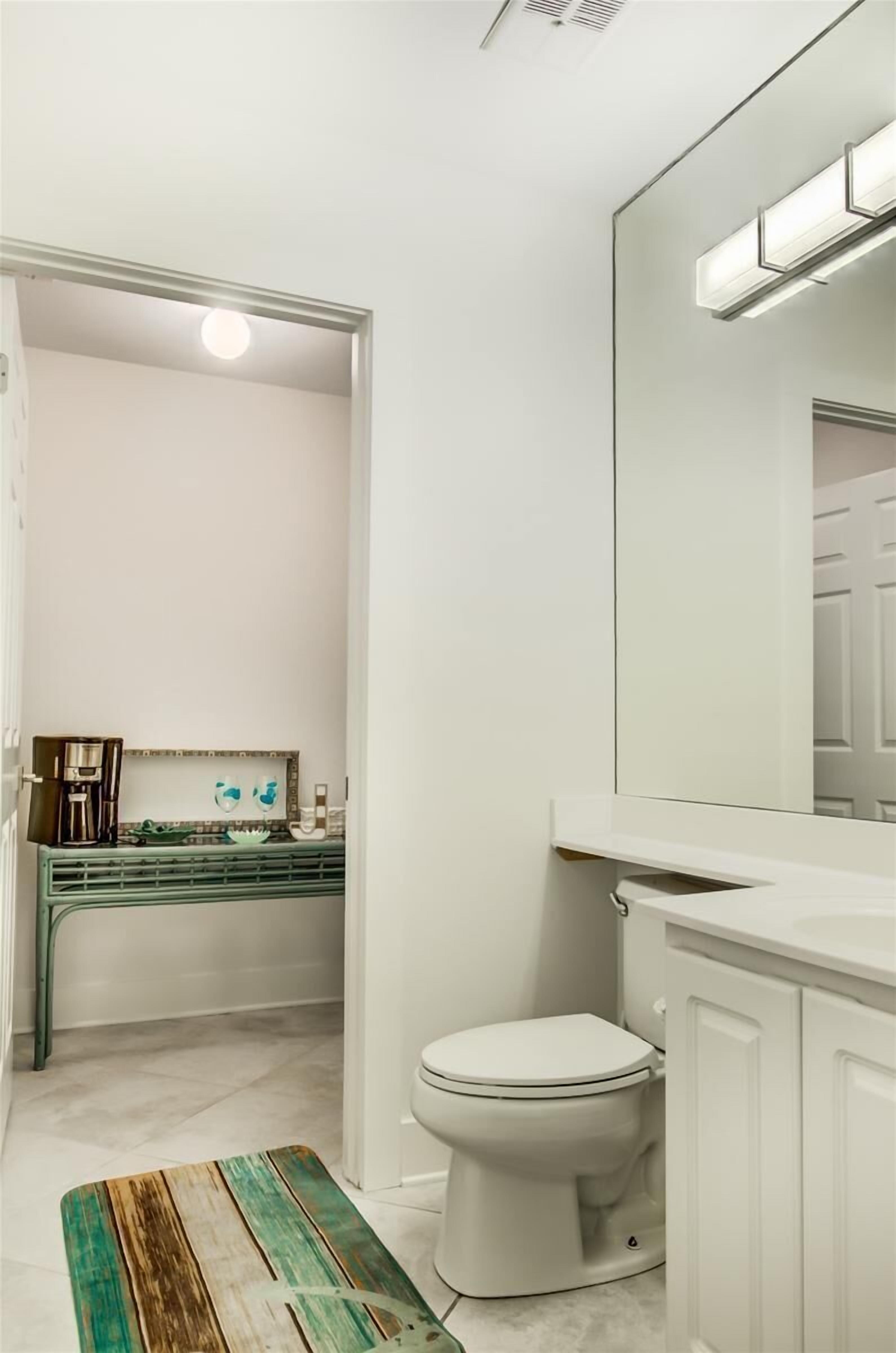 A bathroom with a white toilet, a sink with a green countertop, and a mirror above the sink.