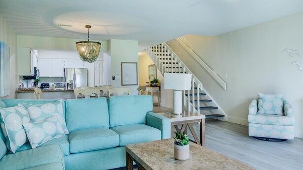 A modern living room with a light blue sofa, a coffee table, and a staircase leading to a kitchen area. - 2C, Stay Salty (Miramar Beach)
