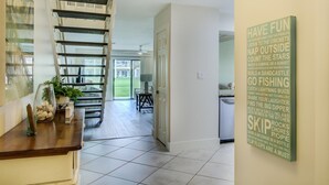 A spacious hallway with a staircase leading to a balcony, a dining area, and a wall with motivational phrases. - 2C, Stay Salty (Miramar Beach)
