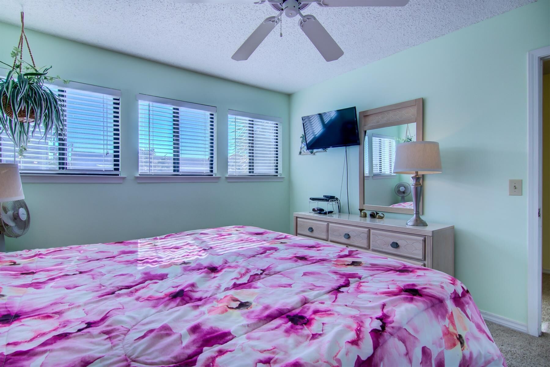 A bedroom with a bed, dresser, TV, and ceiling fan.