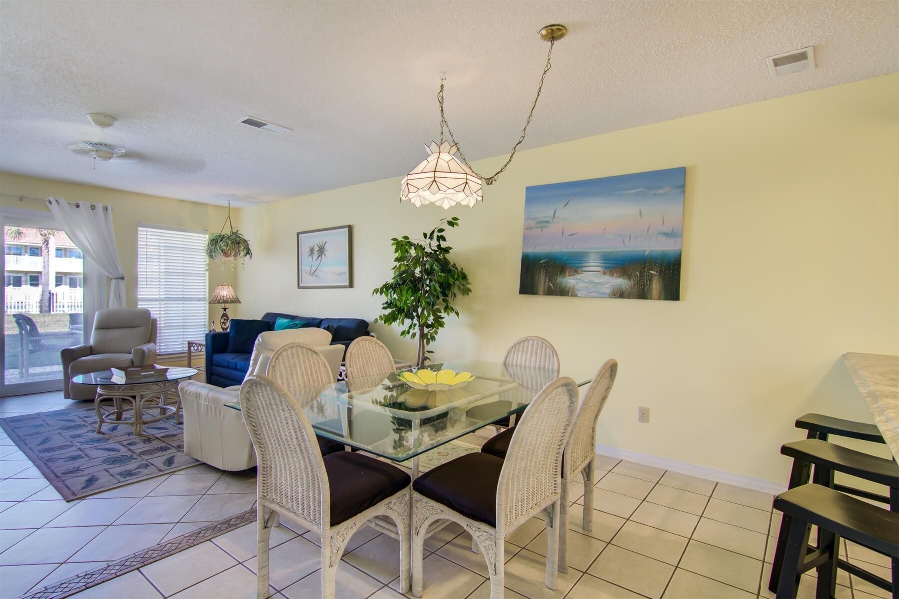 A dining area with a glass table, wicker chairs, and a ceiling light fixture.