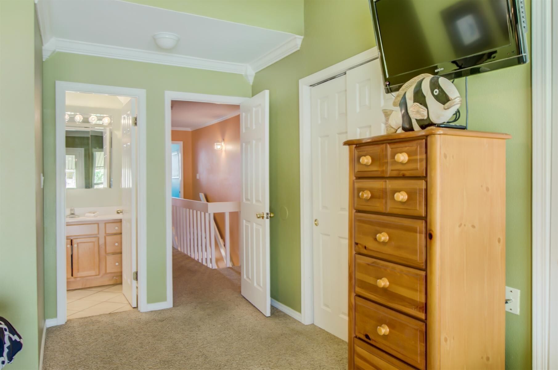 Un couloir avec une commode en bois, un téléviseur fixé au mur et une porte donnant sur une autre pièce.