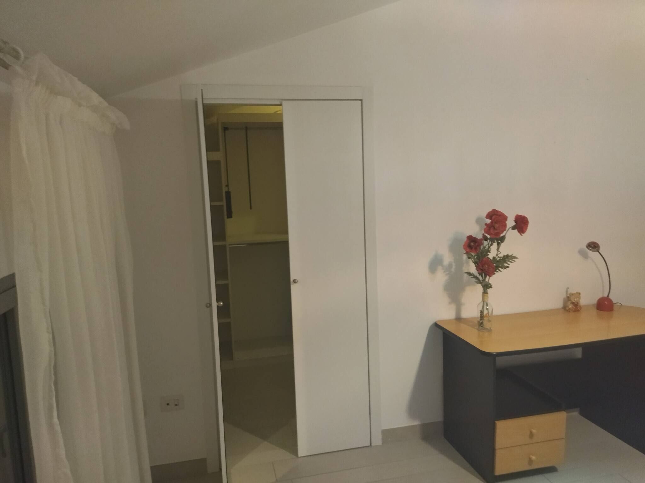 Ein Schlafzimmer mit einem Bett, einem Schreibtisch, einem Stuhl, einem Kleiderschrank und einem Spiegel.