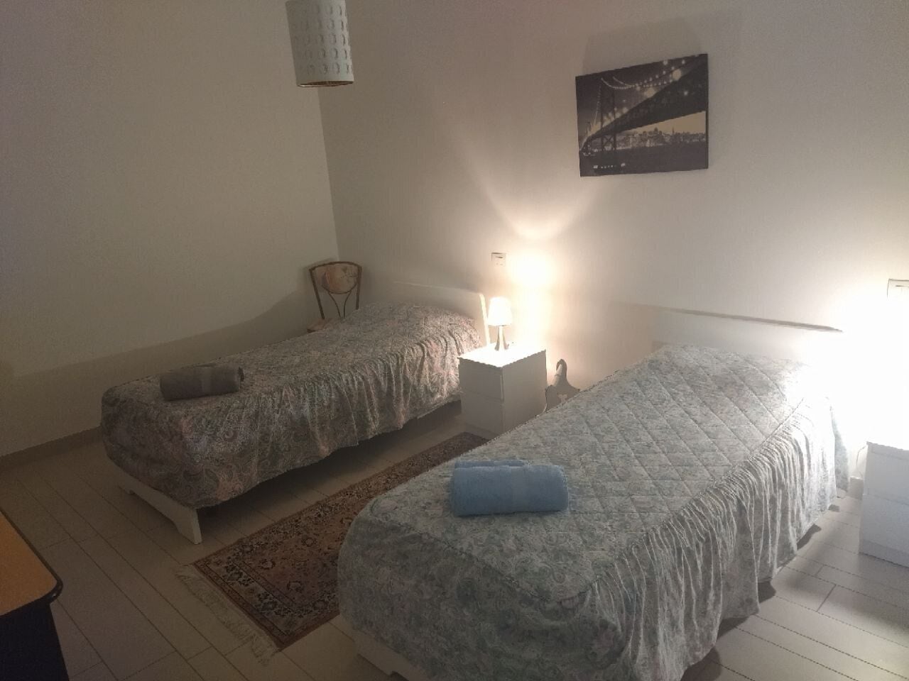 A bedroom with two beds, a nightstand, a chair, and a rug.